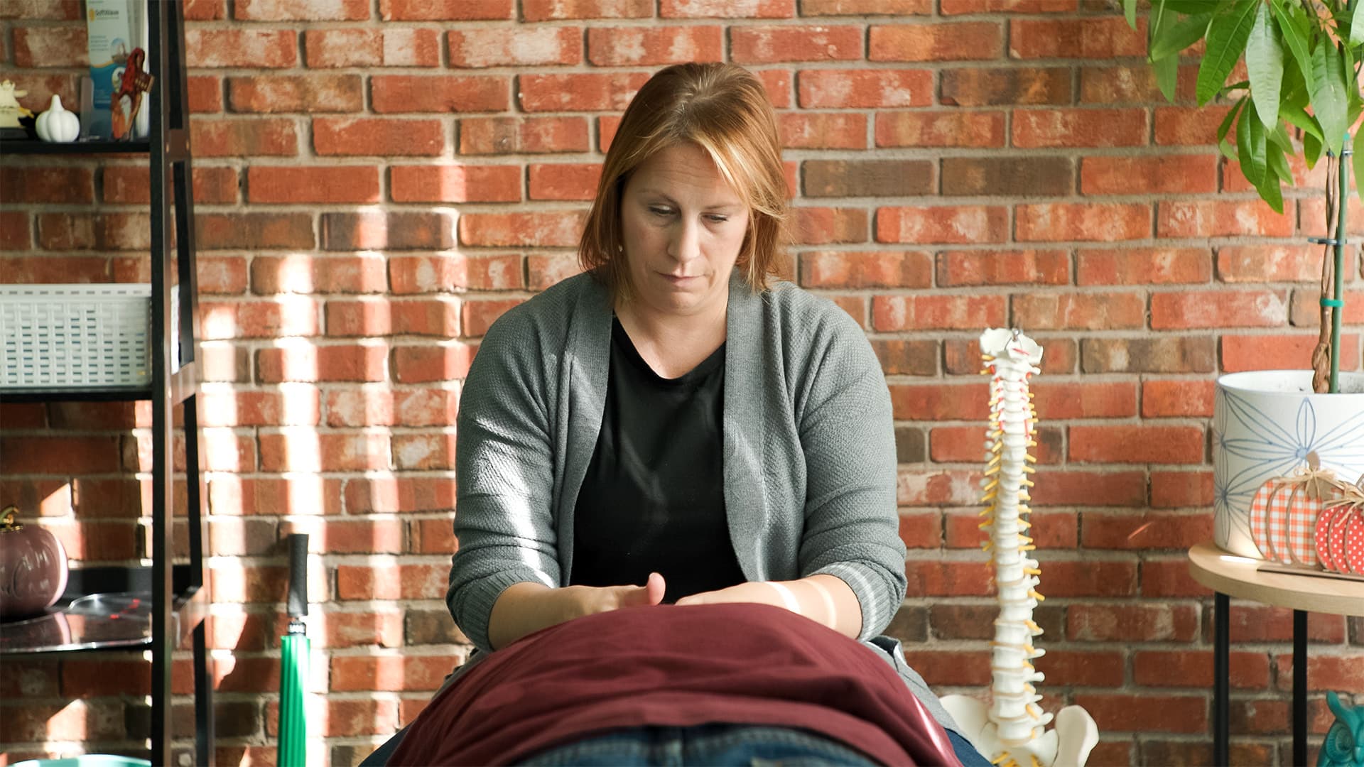 A treatment room at Able Hands Chiropractic, with a brick wall and a spine model beside the table